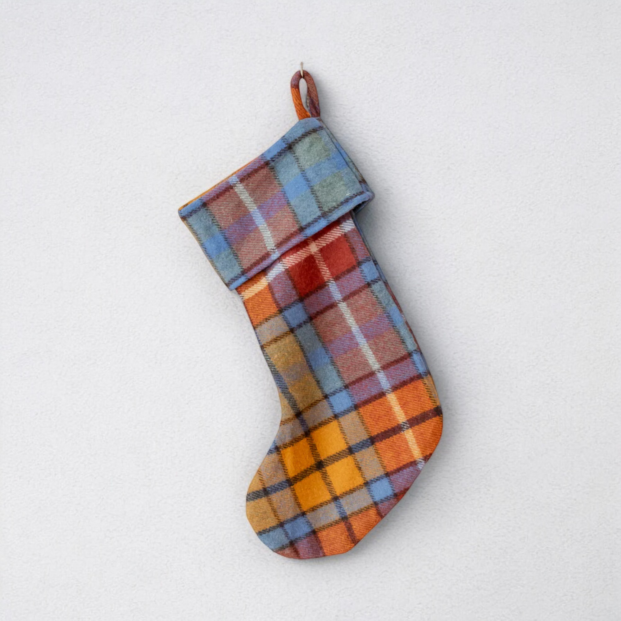 The Antique Buchanan wool Christmas stocking, featuring orange, green, and blue, hung against a white background.