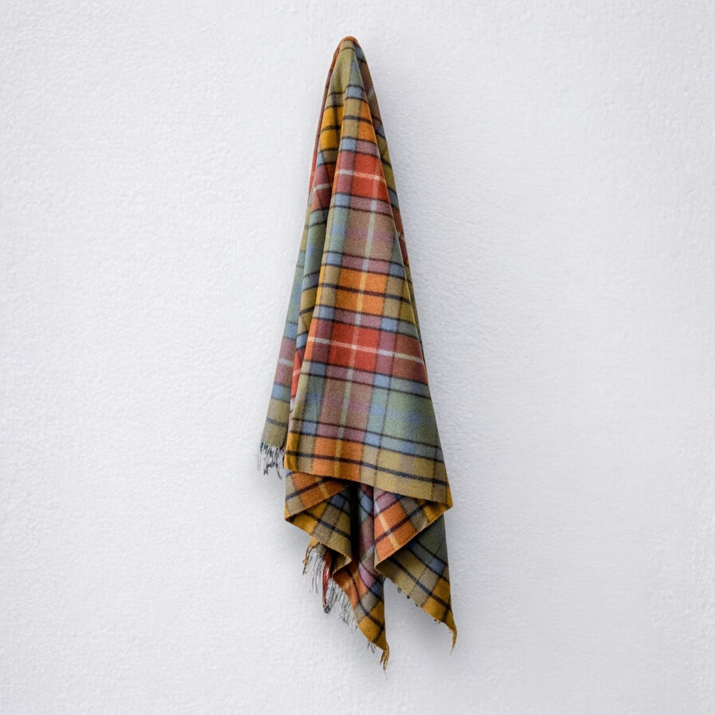 A Buchanan clan tartan blanket with fringing, hanging against a white background.