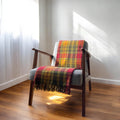 A  autumn buchanan recycled wool tartan knee blanket with fringed edges draped over a wooden chair in a room with a light interior.