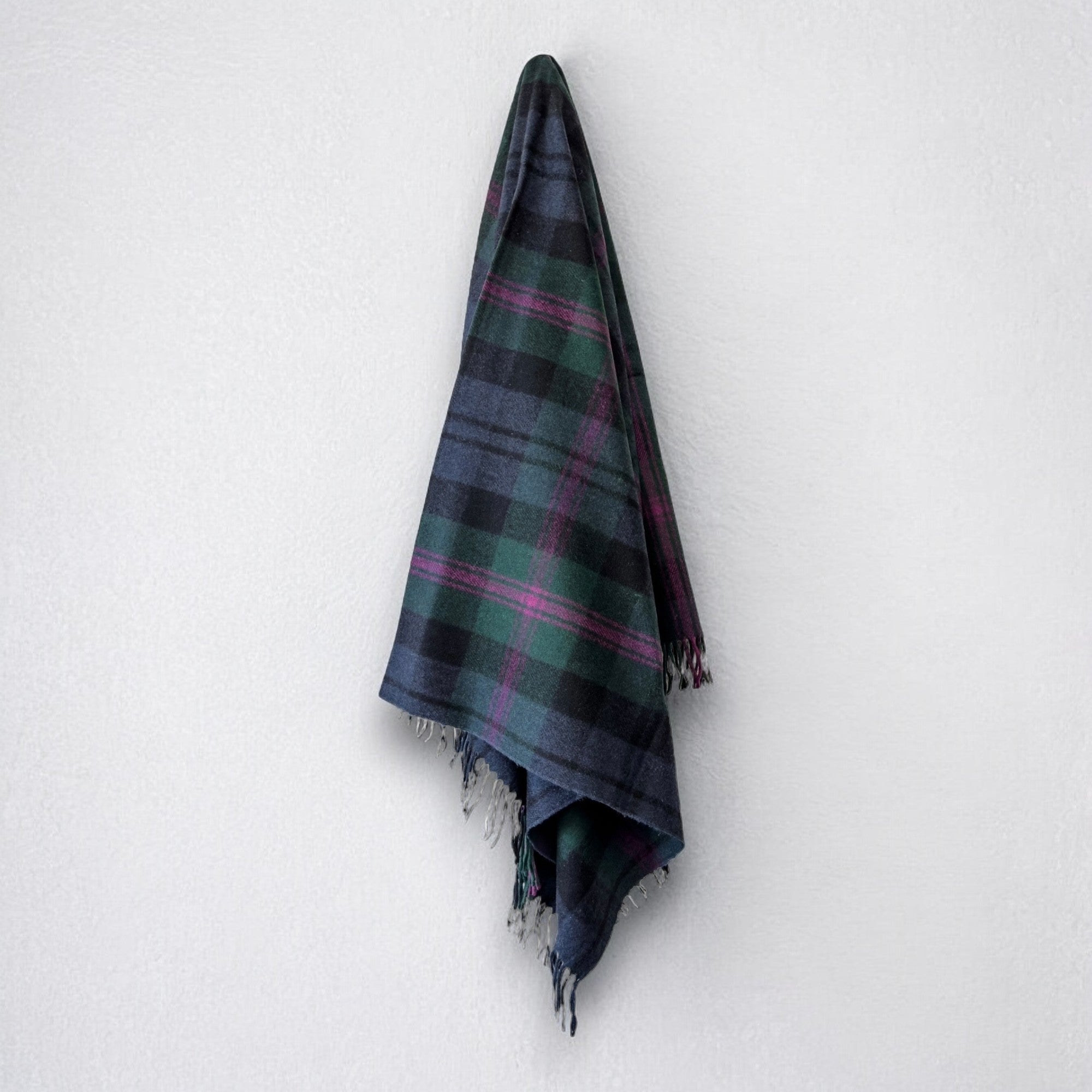a 100% recycled blanket in baird tartan hanging from a wall hook on a white background 