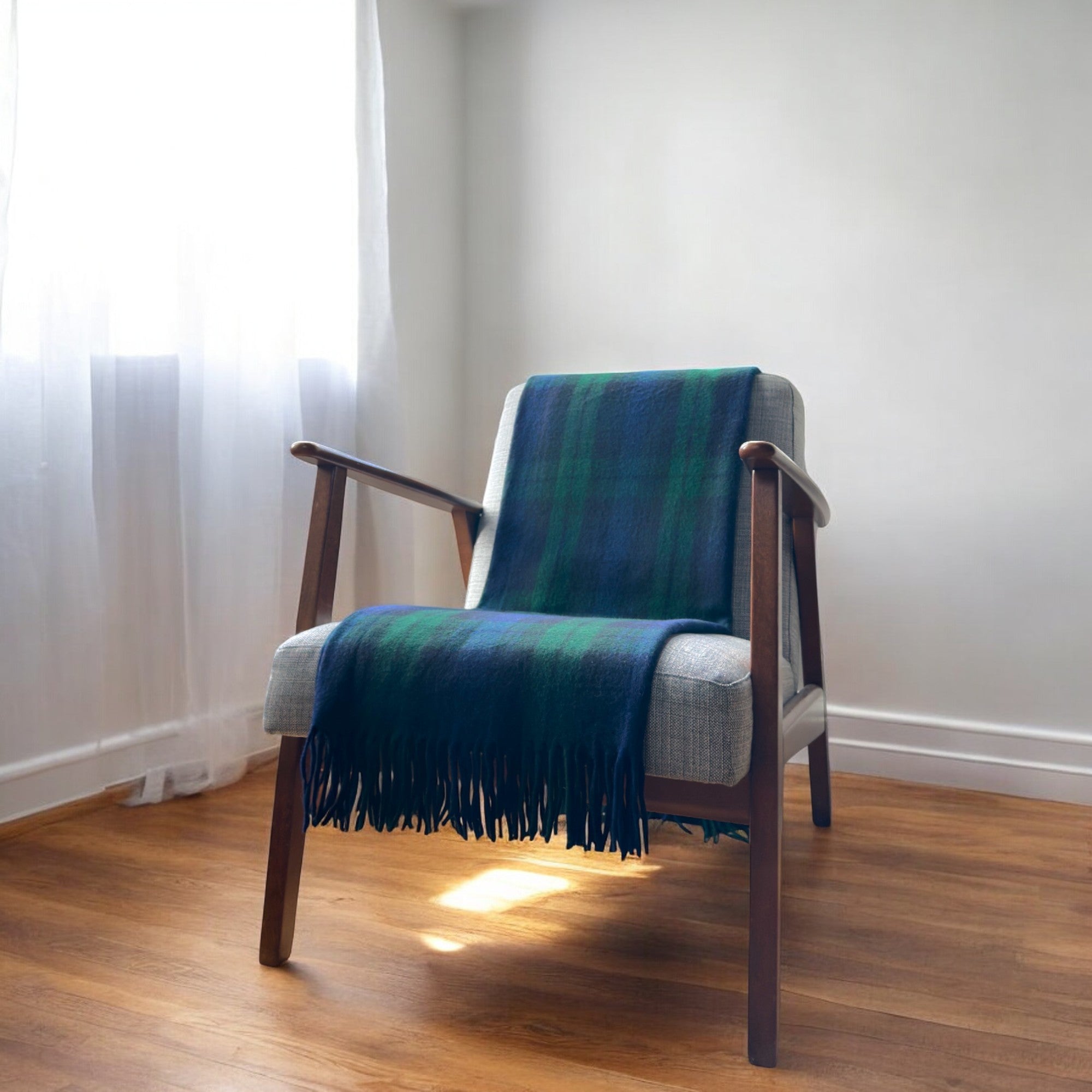 A blackwatch recycled wool tartan knee blanket with fringed edges draped over a wooden chair in a room with a light interior.