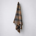 a 100% recycled blanket in camel thomson tartan hanging from a wall hook on a white background