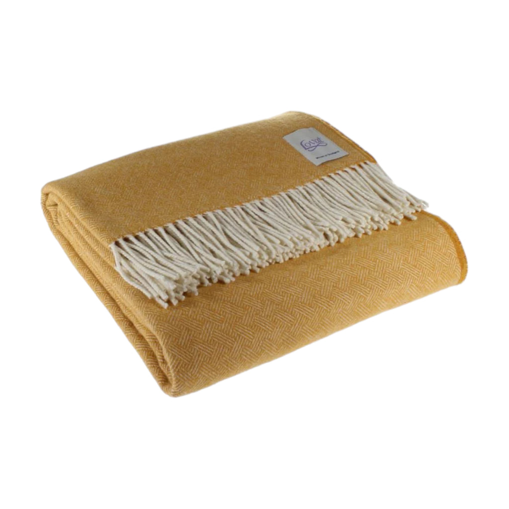 A folded 100% lambswool diamond border blanket in harvest yellow with fringing, displayed on a neutral background.