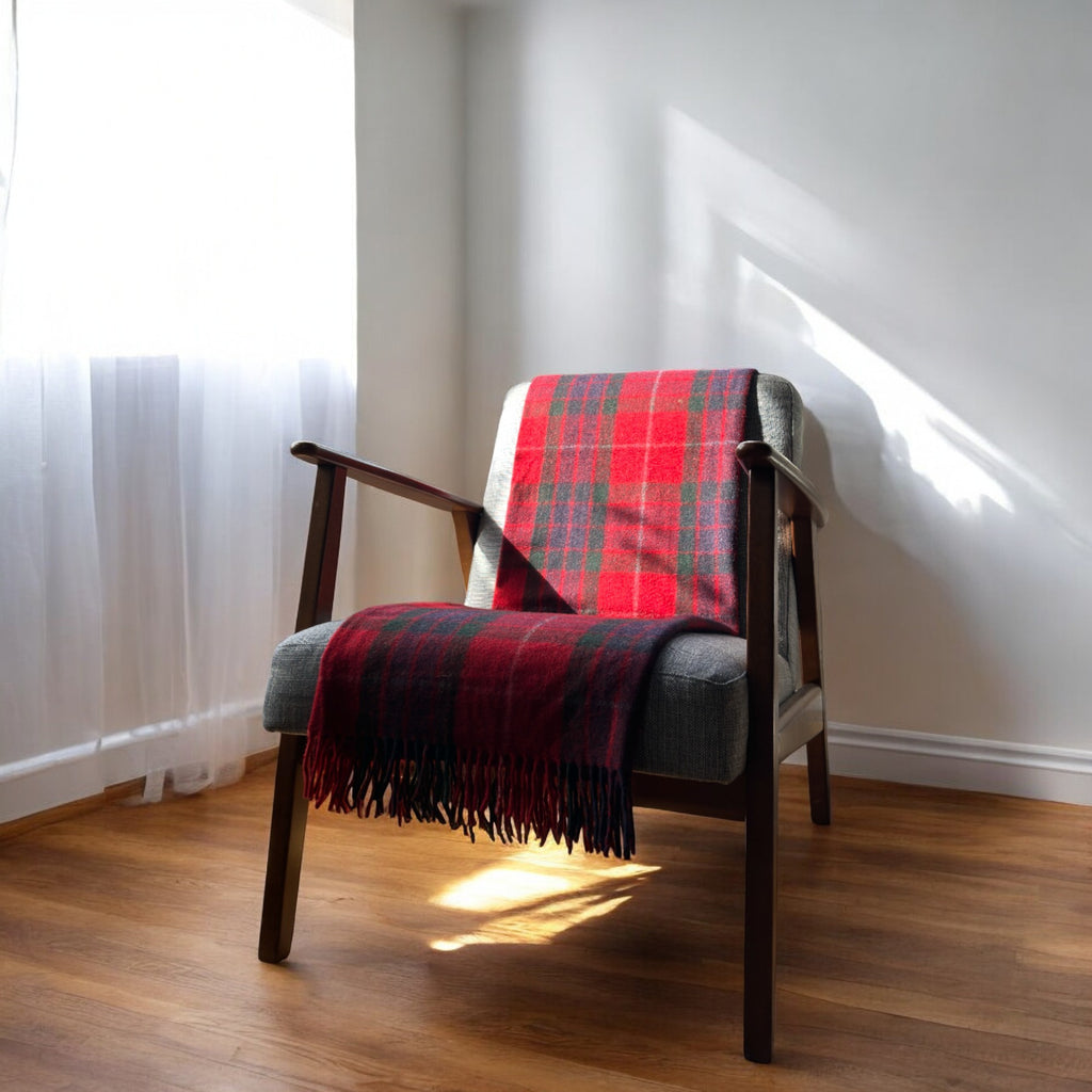 A fraser recycled wool tartan knee blanket with fringed edges draped over a wooden chair in a room with a light interior.