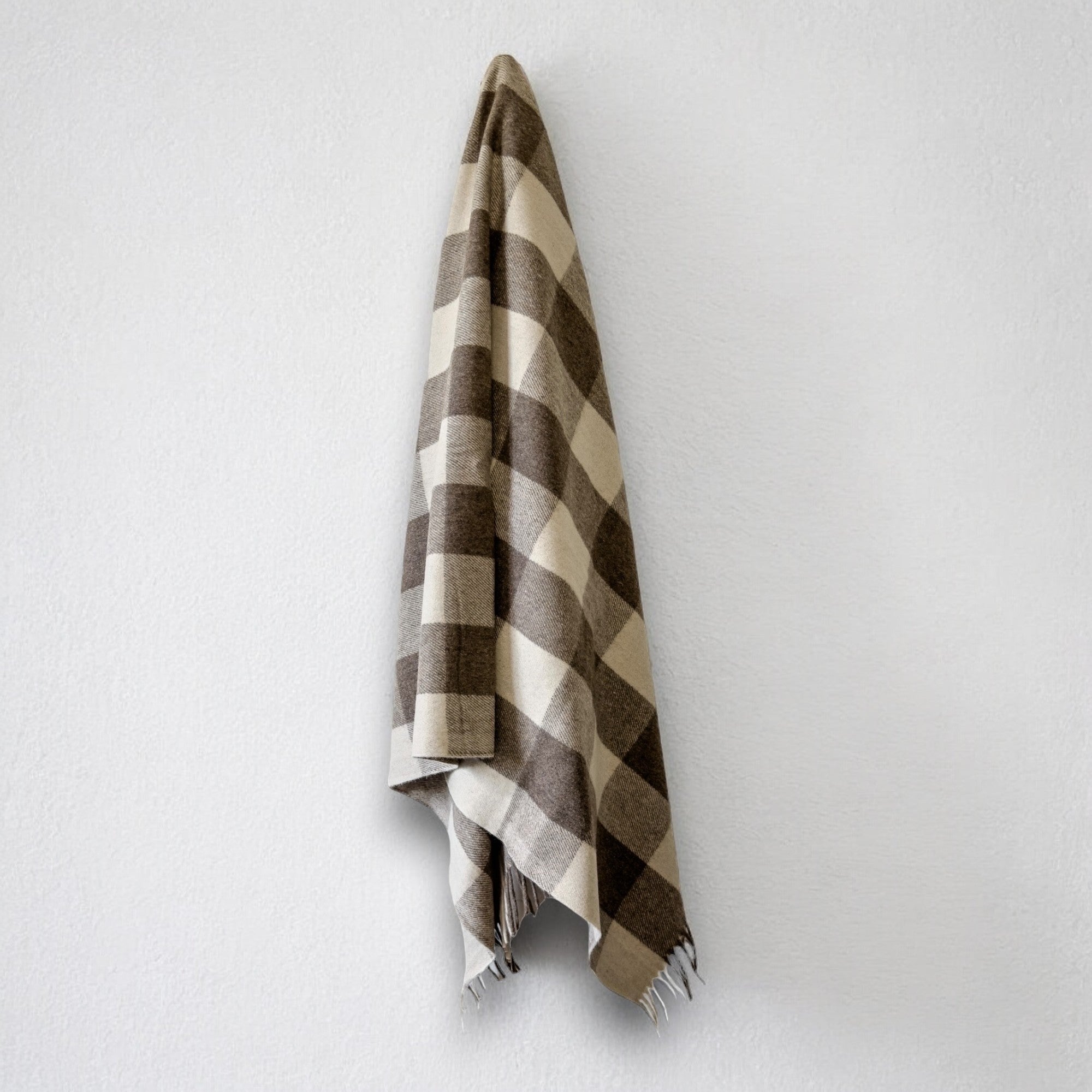 a 100% recycled blanket in jacob tartan hanging from a wall hook on a white background 
