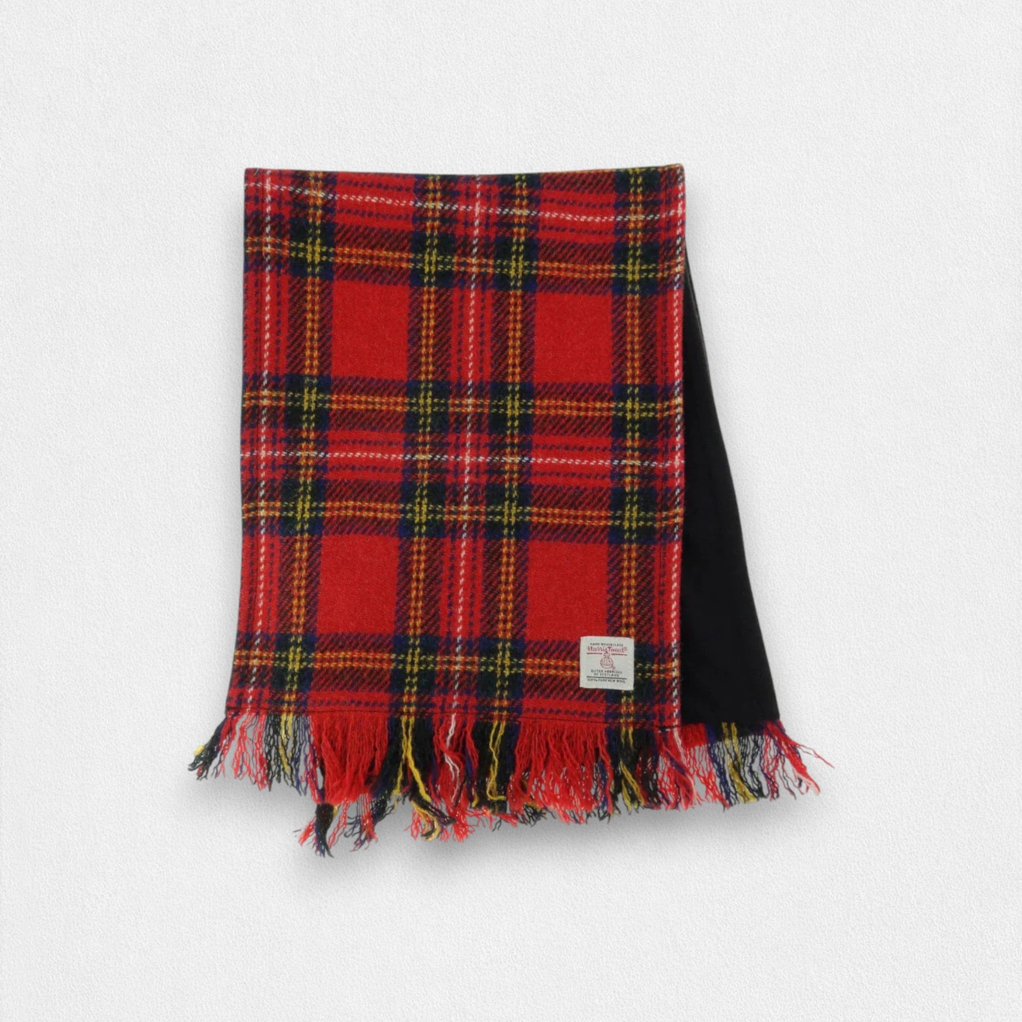 A Harris Tweed scarf with a red and blue tartan pattern, featuring fringes and a label showing the brand name.