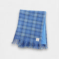 A sky blue check Harris Tweed scarf with fringing, laid flat.