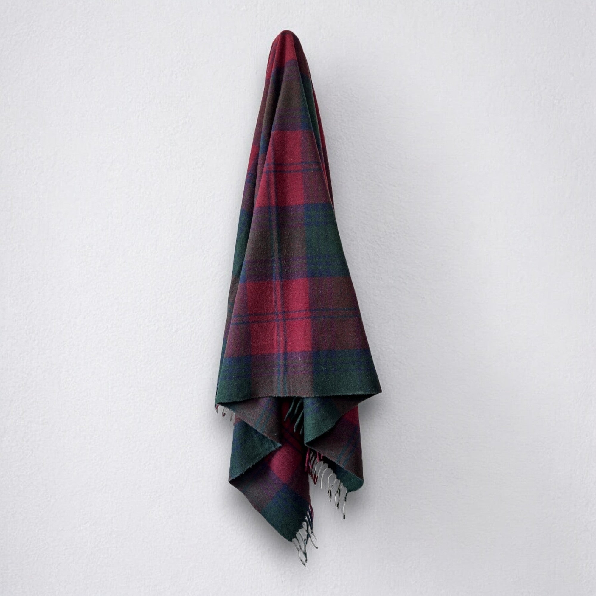 a 100% recycled blanket in lindsay tartan hanging from a wall hook on a white background 