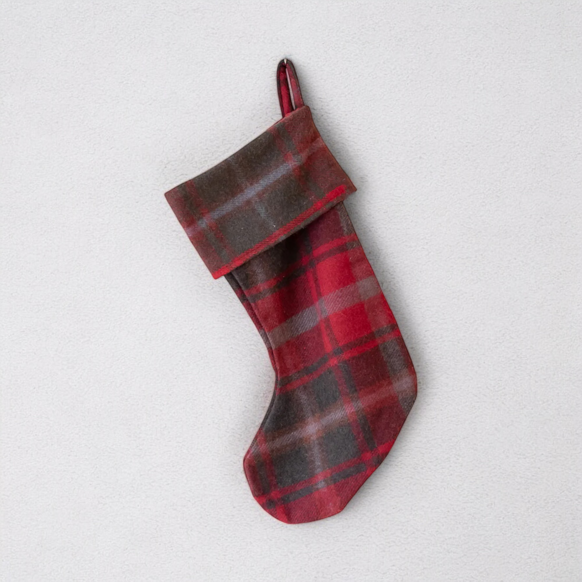 A red and dark brown plaid Maple Christmas stocking, hanging against a white background.