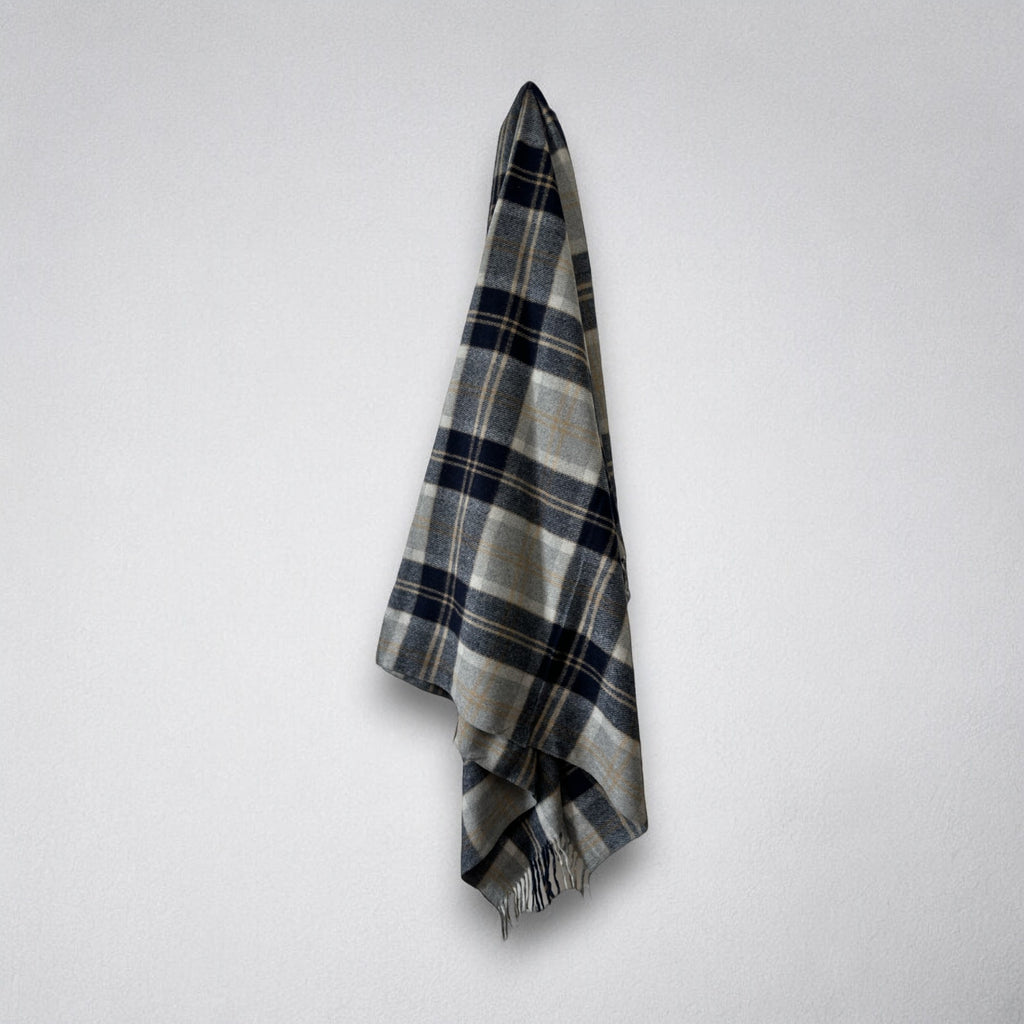 A Silver Bannockbane tartan patterned blanket draped over a white wall, with fringing visible on the ends.