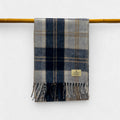 A silver bannockbane scarf with fringes, displayed on a yellow rod against a white wall.