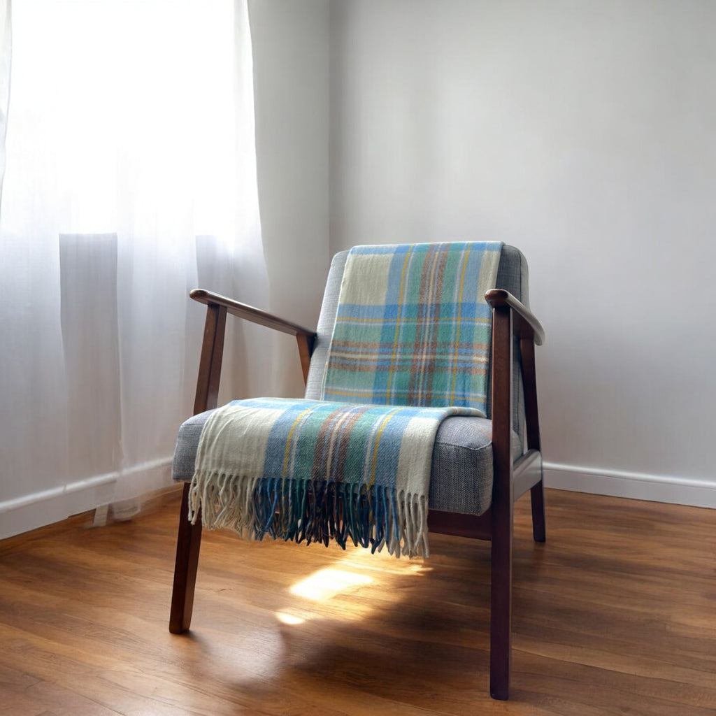 a 100% recycled blanket in stewart muted blue tartan draped over a chair in a cosy room