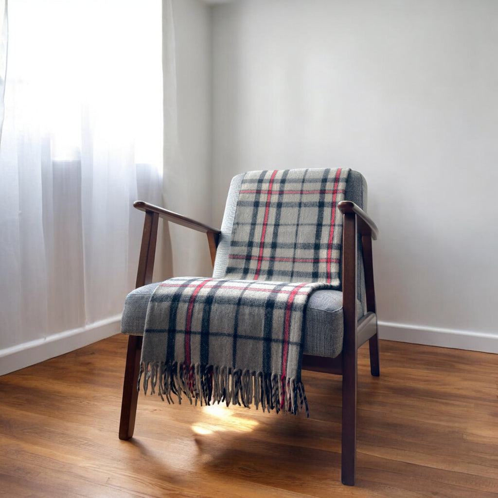 a 100% recycled blanket in thomson grey tartan draped over a chair in a cosy room