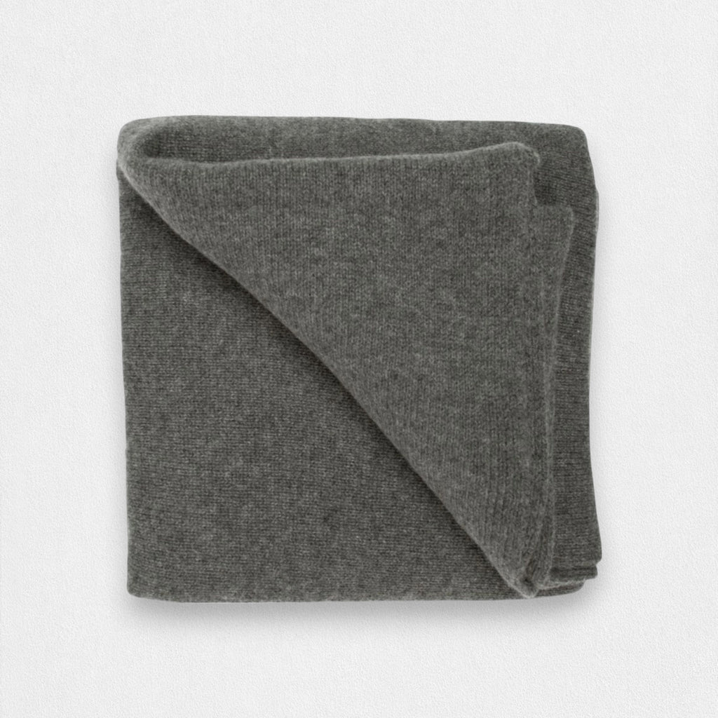 A folded dark grey cashmere blanket displayed on a surface.